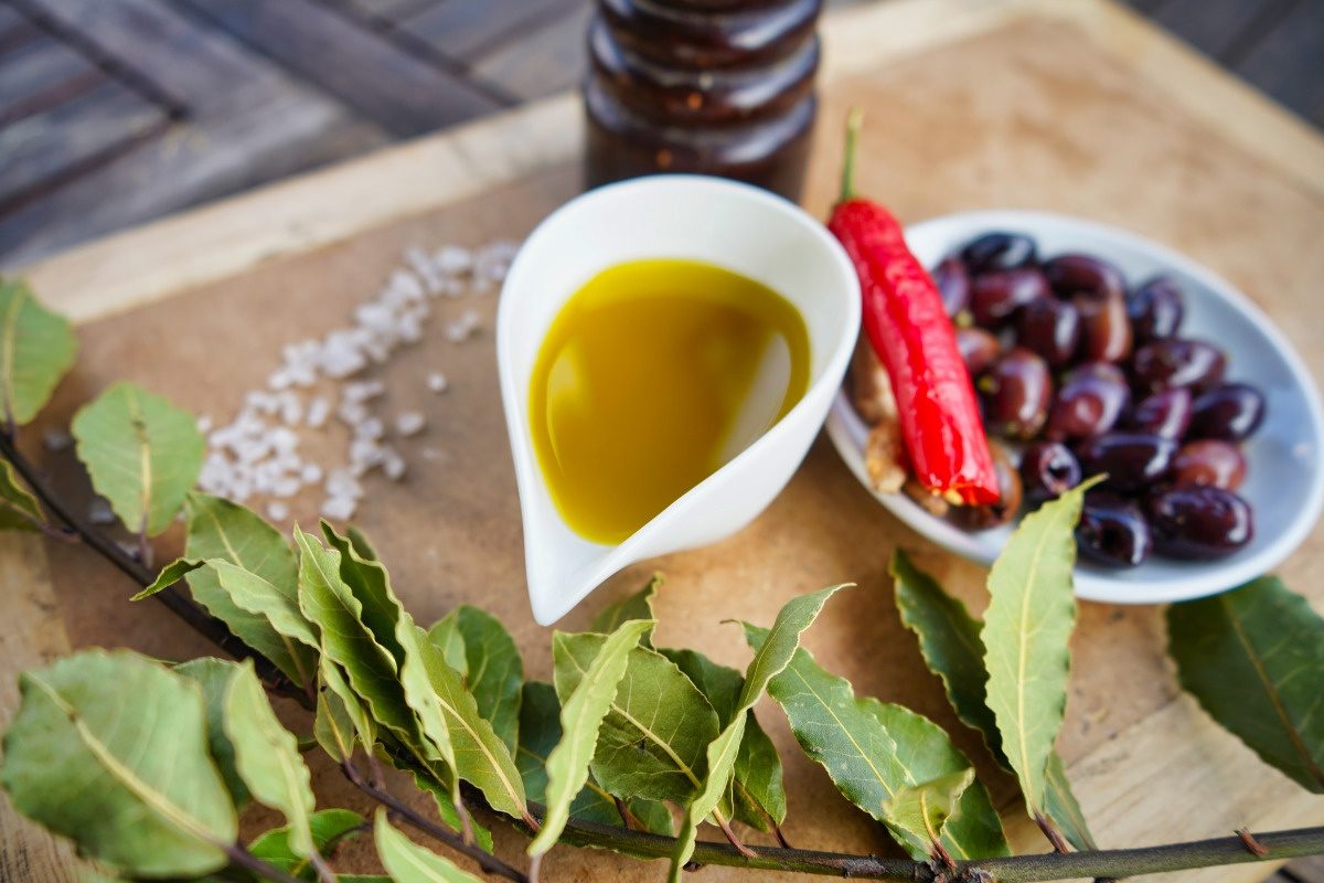Vita verde Olivenöl in Schale mit Oliven und Blättern auf Brett